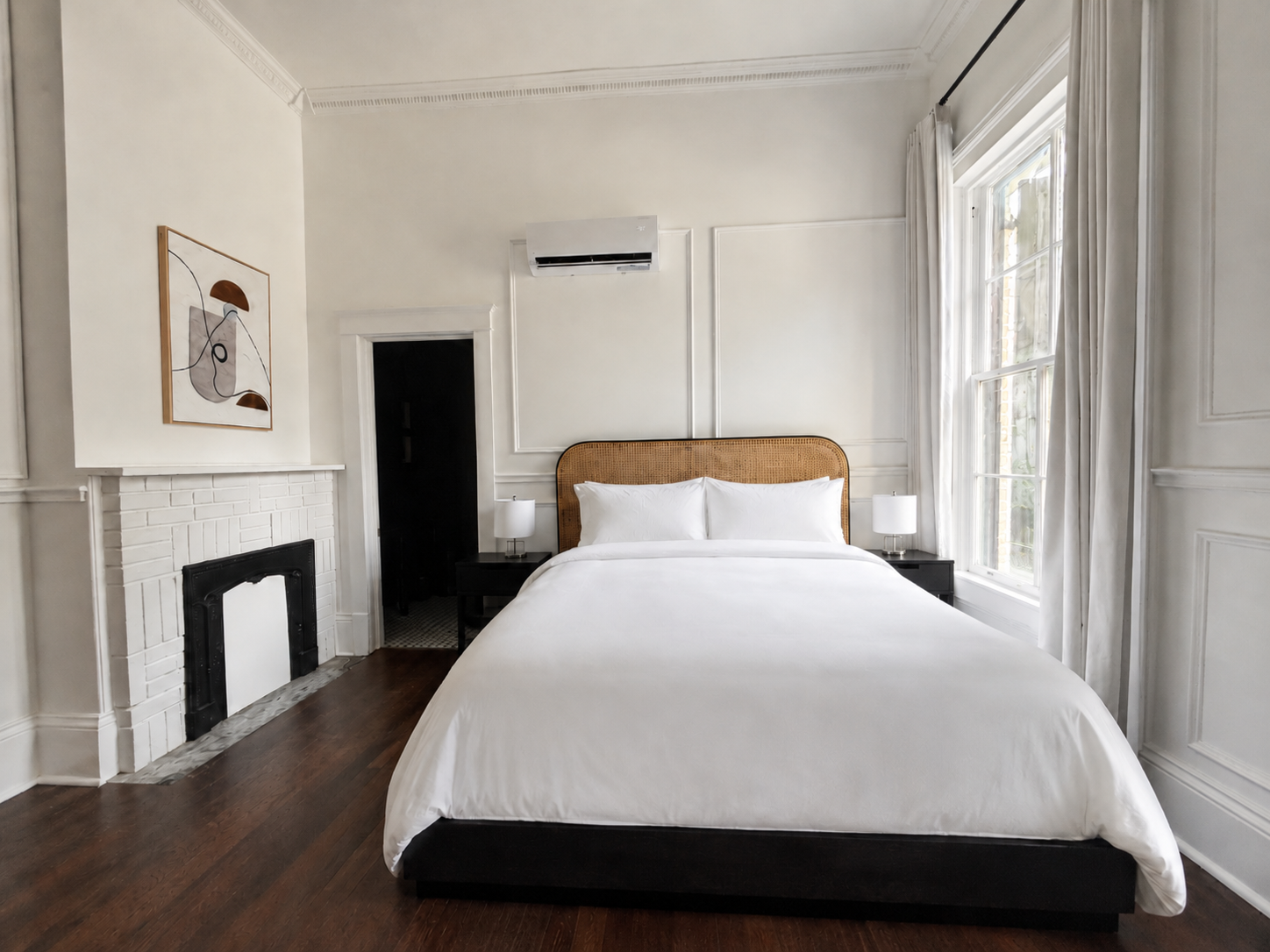 Minimal white bedroom with a bed, fireplace, tall window, and framed art.