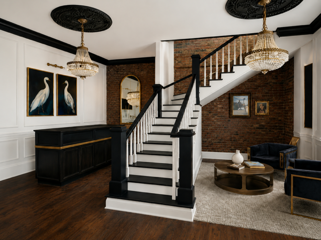 Stylish foyer with black-and-white staircase, dark wood floor, brick accent wall, and gold chandeliers.