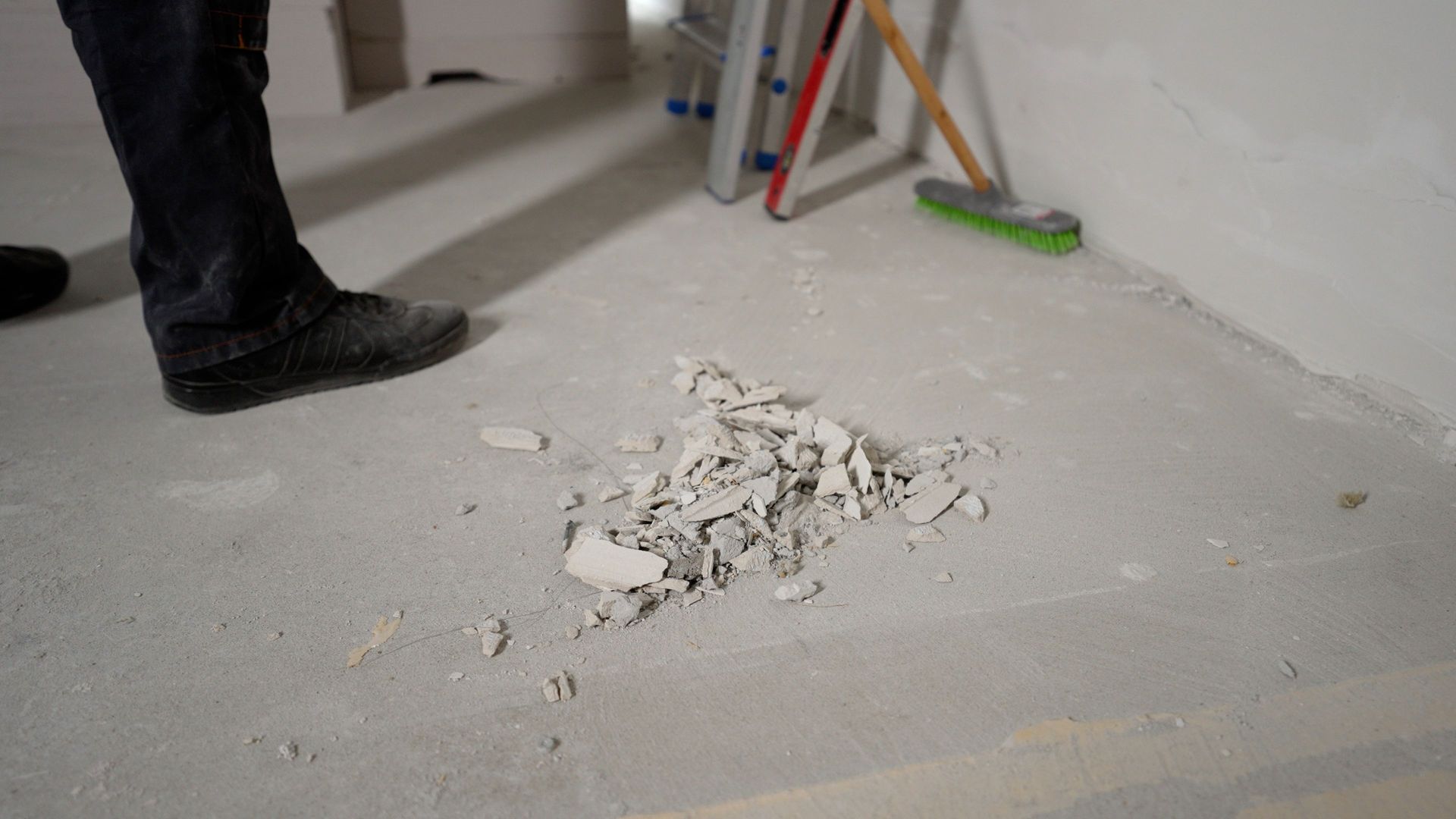 A person is standing next to a pile of concrete on the floor.