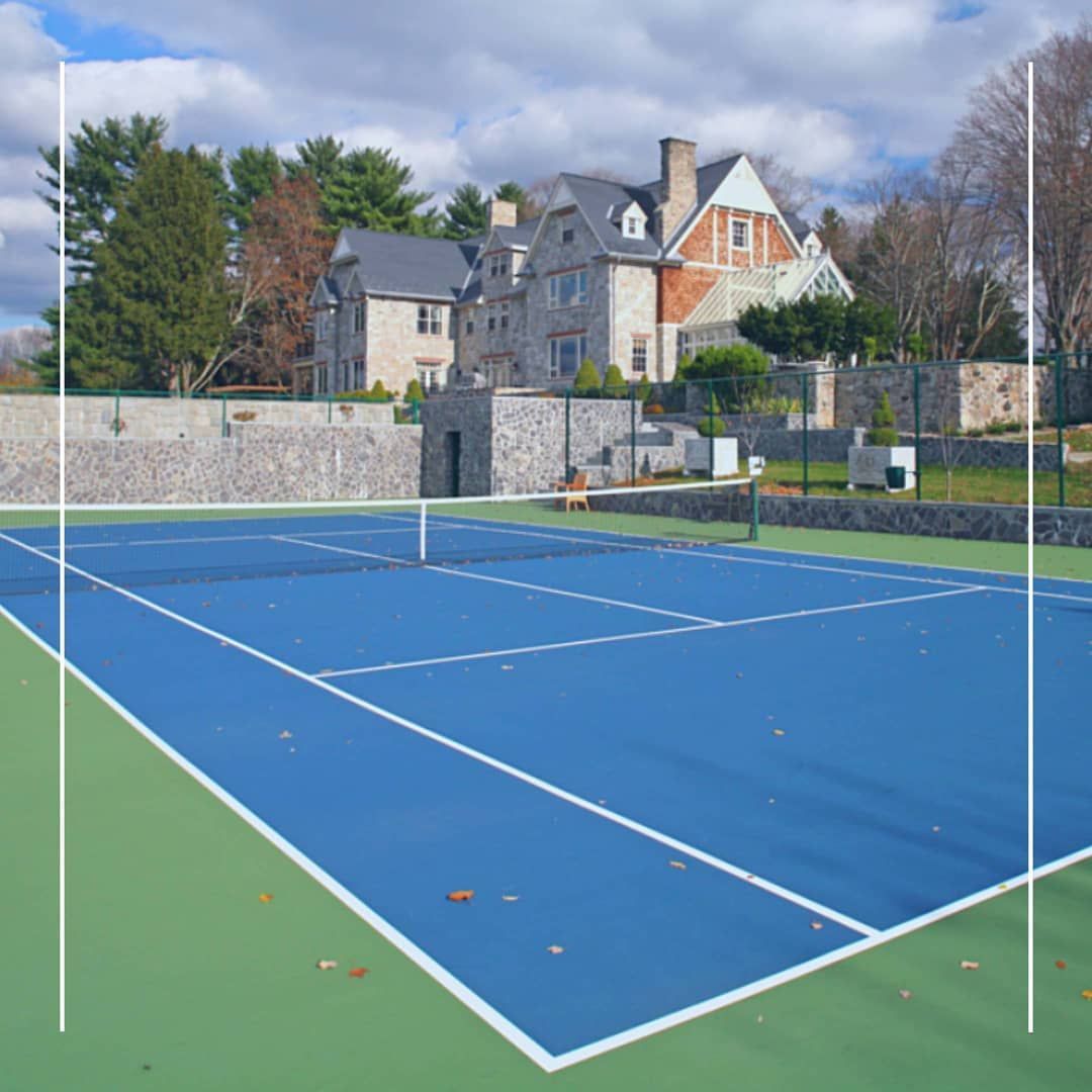 Blue tennis court with a large stone mansion in the background on a sunny day.