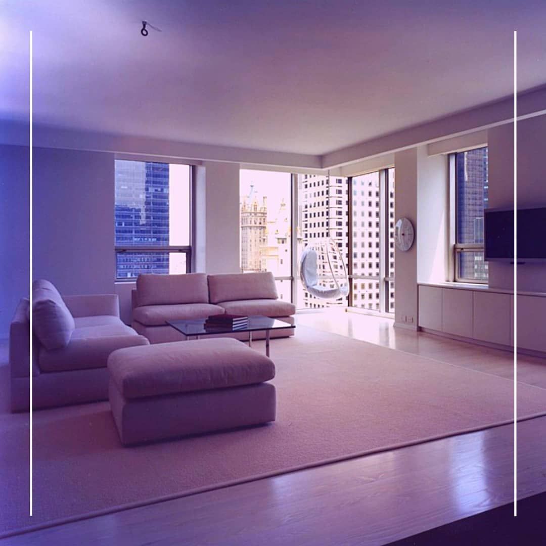 Modern living room with city view, light-colored furniture, large windows, and a hanging chair.