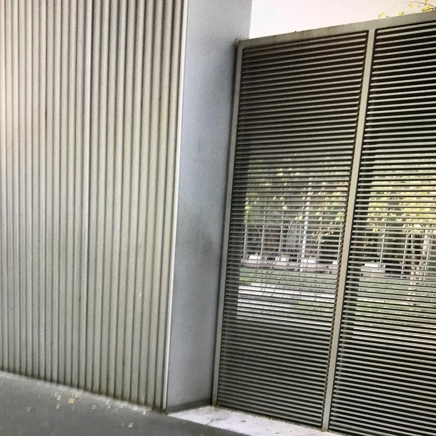 Exterior building with vertical ribbed siding and slatted doors; green trees reflected.