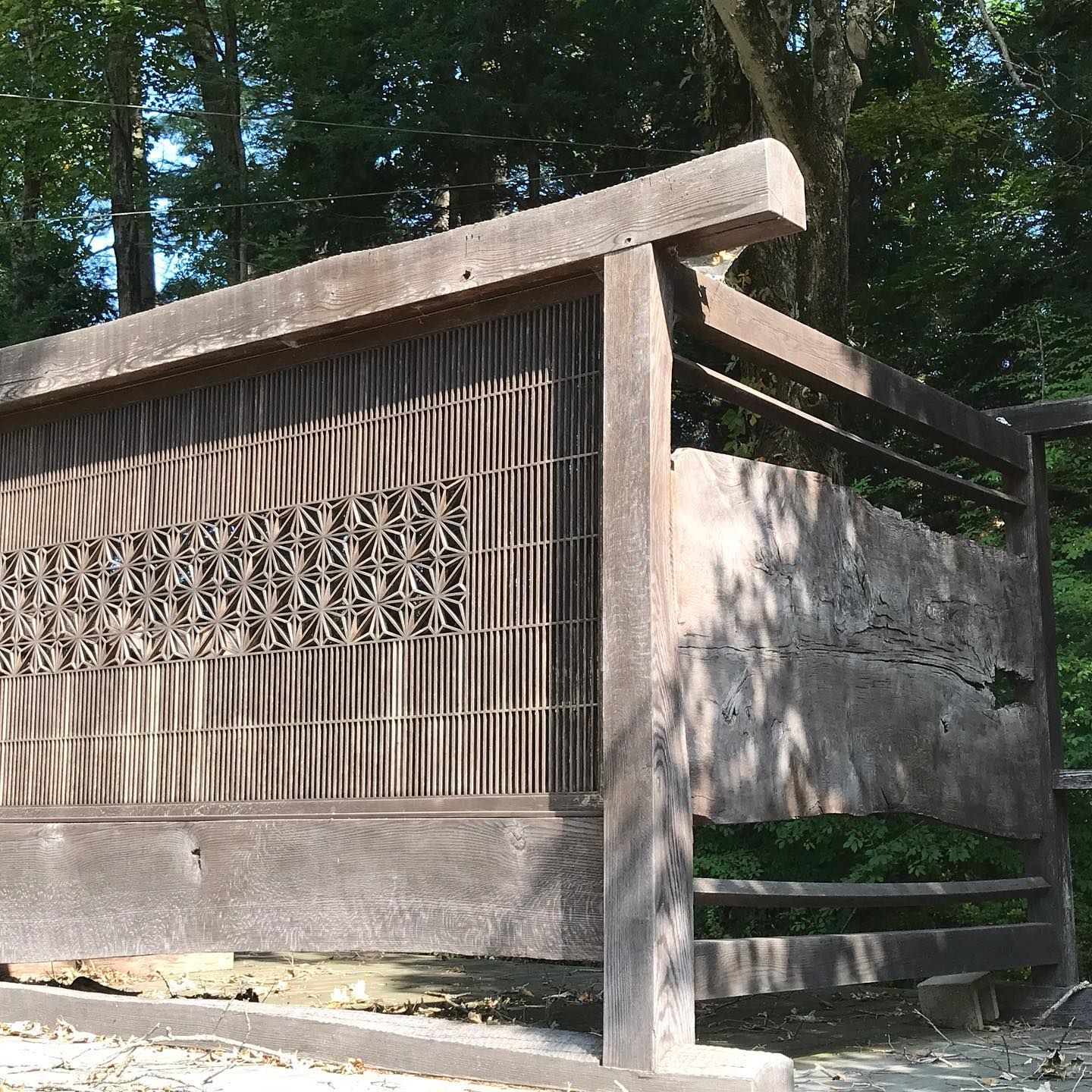 Wooden fence with textured panels and geometric cutout, in a park setting.