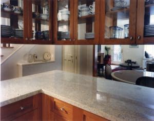 Kitchen with light granite countertop, wooden cabinets, and glass-fronted upper cabinets displaying dishware.