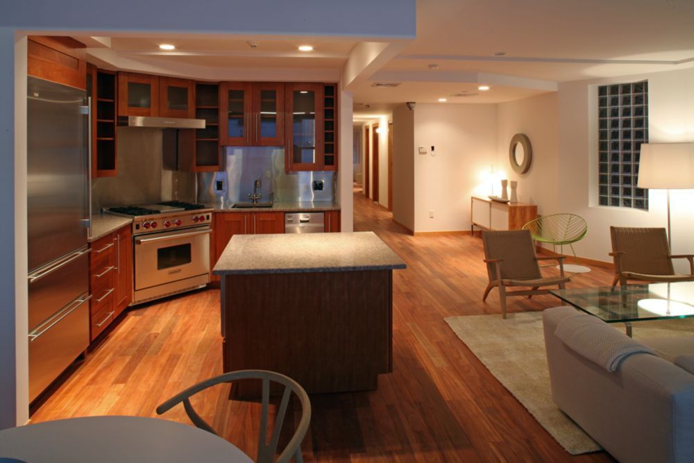 Modern kitchen and living space with wood cabinets, island, and stainless steel appliances.
