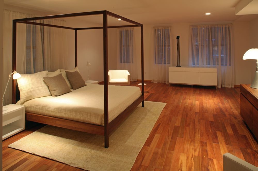 Modern bedroom with hardwood floors, canopy bed, white furniture, and sheer curtains.