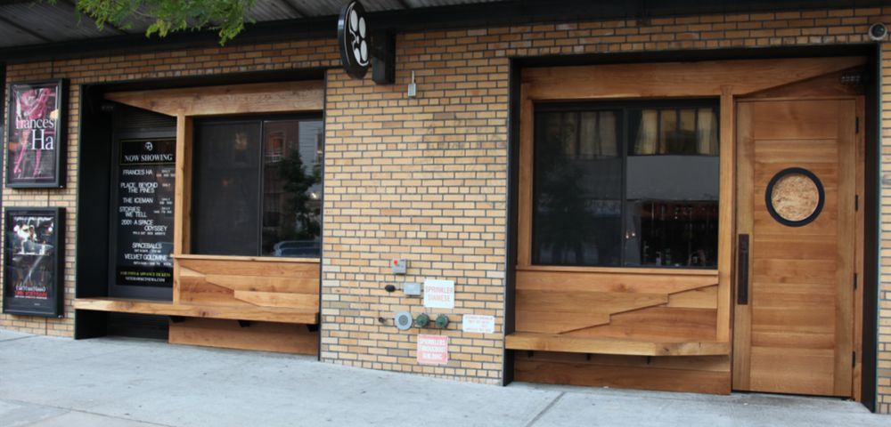 Exterior view of a brick building with wooden accents, including windows and a door with a round window.