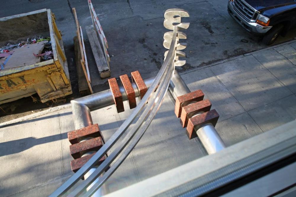 Outdoor handrail with brick supports, silver metal. A dumpster and vehicle are visible in the background.