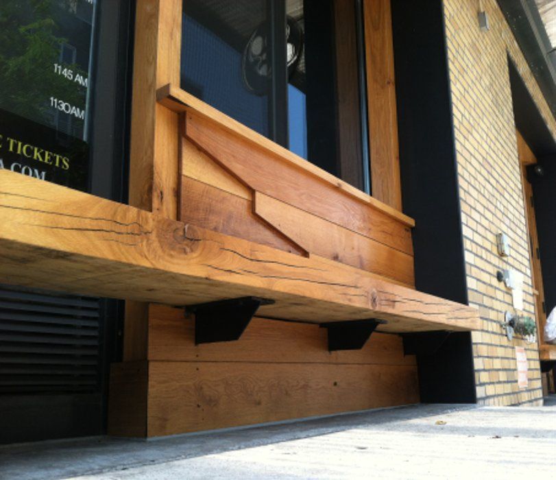 Wooden window frame with an attached bench supported by black metal brackets on a building's facade.