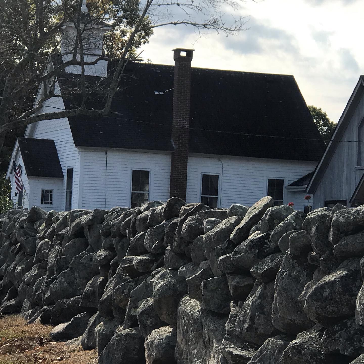 White clapboard church with black roof and brick chimney behind a stone wall.