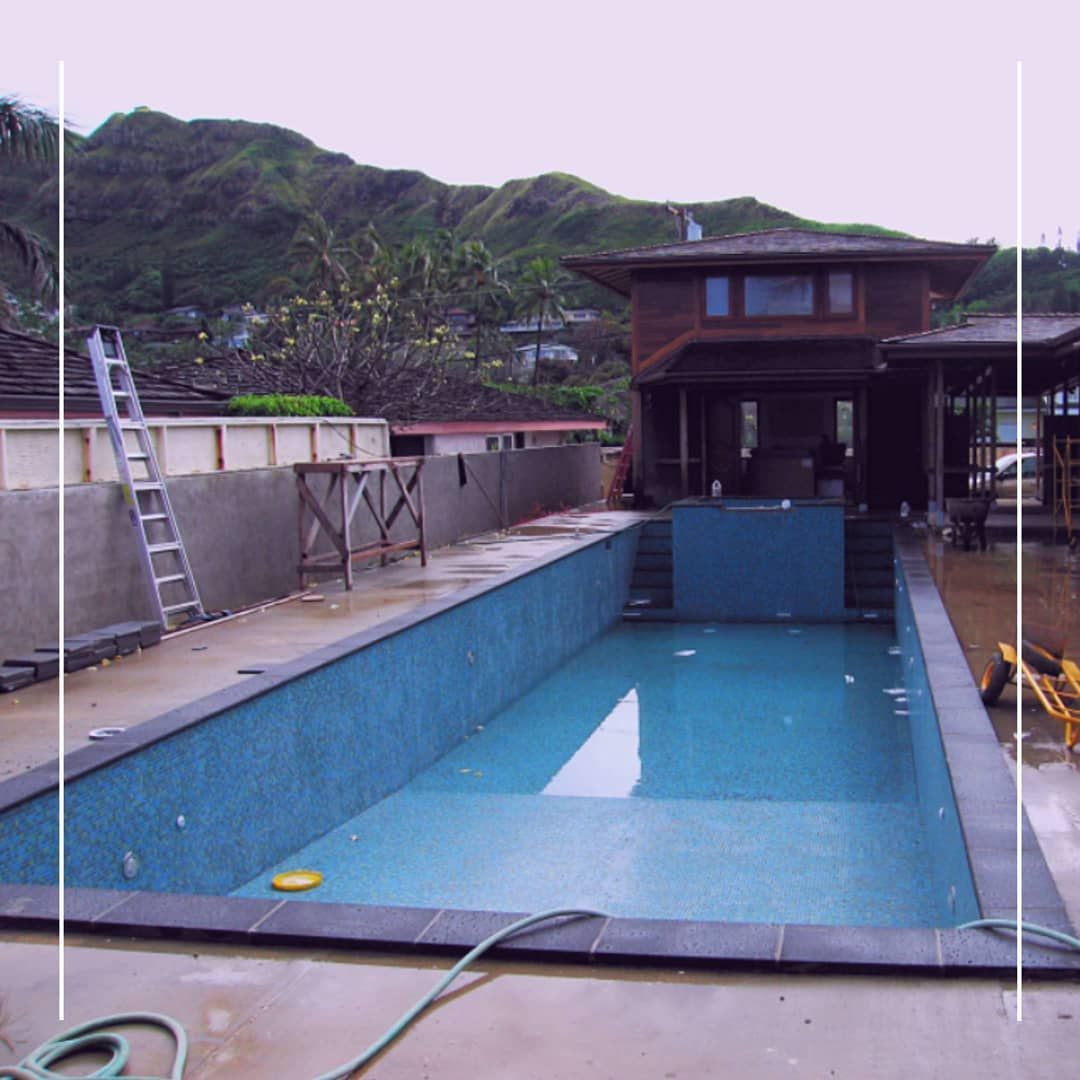 Pool under construction with house, ladder, and mountains in the background.