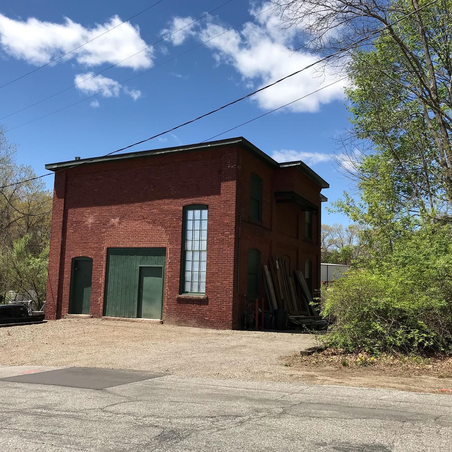 Red brick building with green doors and windows under a blue sky, gravel lot in front.