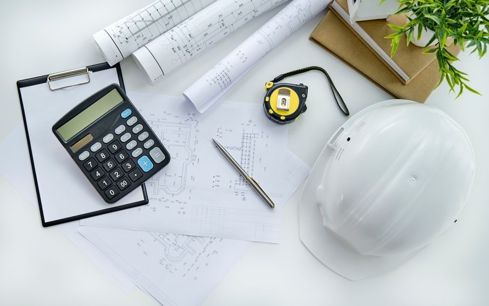 Construction tools including a hard hat, blueprints, calculator, and measuring tape on a white surface.