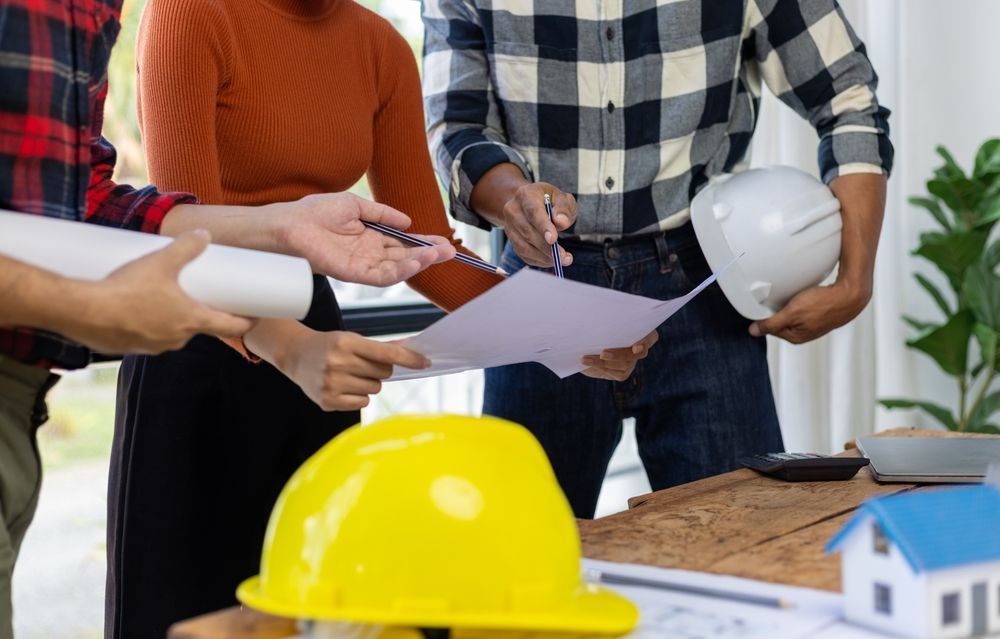 Construction team reviewing blueprints; hard hats, model house, papers on table.