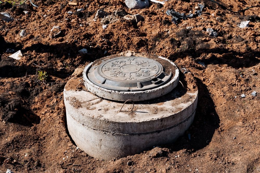 Concrete septic tank with lid in brown soil.
