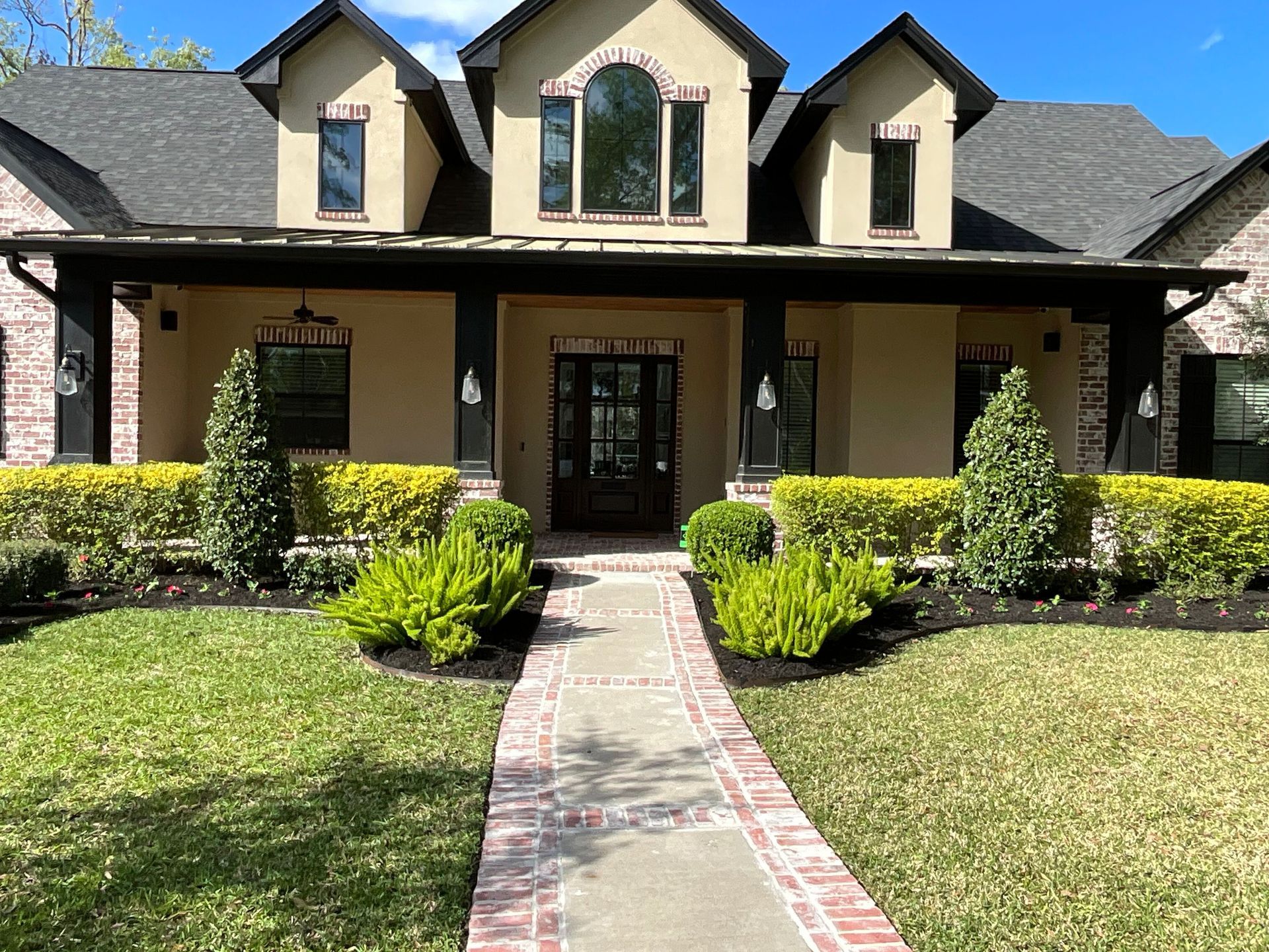 Front view of a beige house with a dark roof, front walkway, and landscaped yard on a sunny day