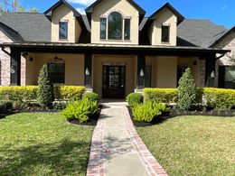 Front view of a beige house with a dark roof, front walkway, and landscaped yard on a sunny day