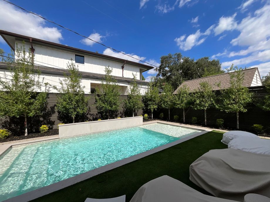 Modern courtyard with a turquoise pool, white two-story building, and lounge chairs under a blue sky