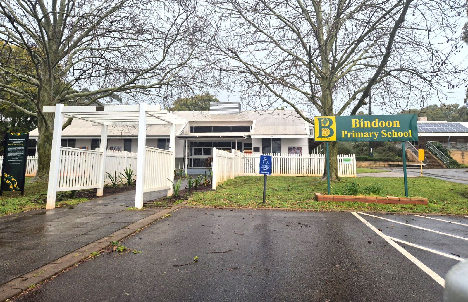 Bindoon Primary School entrance on a cloudy day, with a white fence, sign, and driveway.