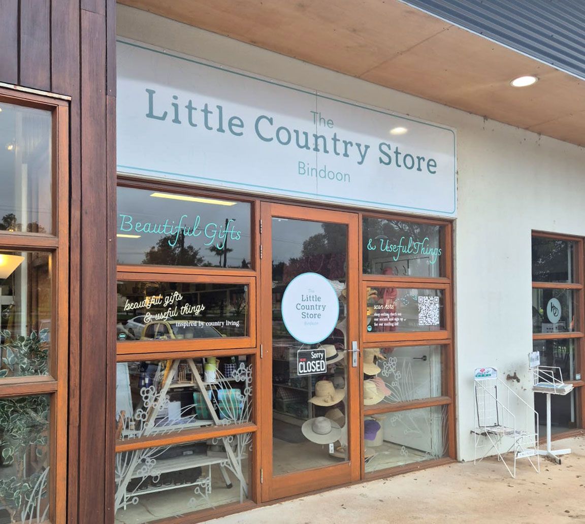 The Little Country Store in Bindoo with a light-colored awning, glass door & windows, displaying hats and merchandise.