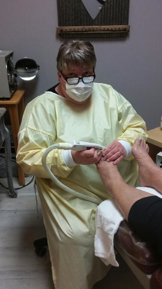 A woman wearing a mask is sitting in a chair giving a foot treatment to a patient.