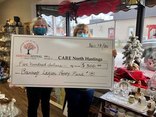 Two women wearing masks are holding a large check in a store.