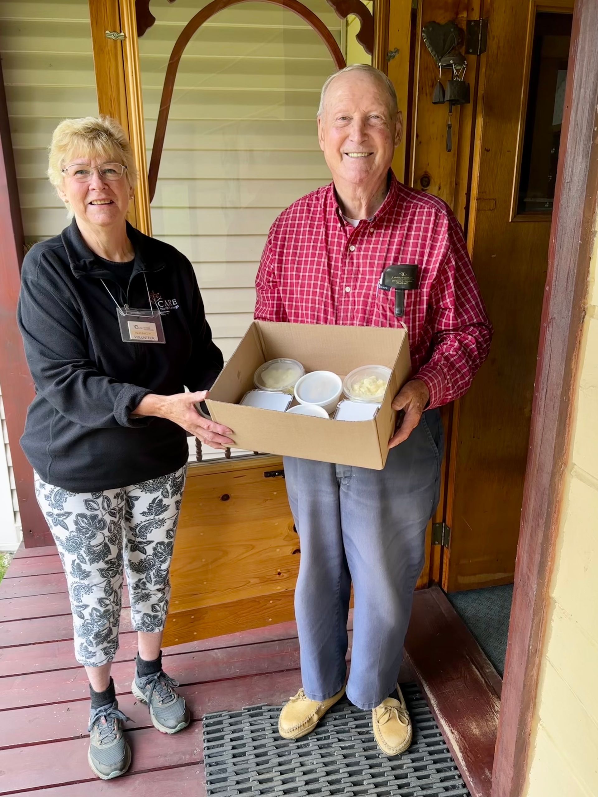 A man and a woman are standing next to each other holding a box of food.