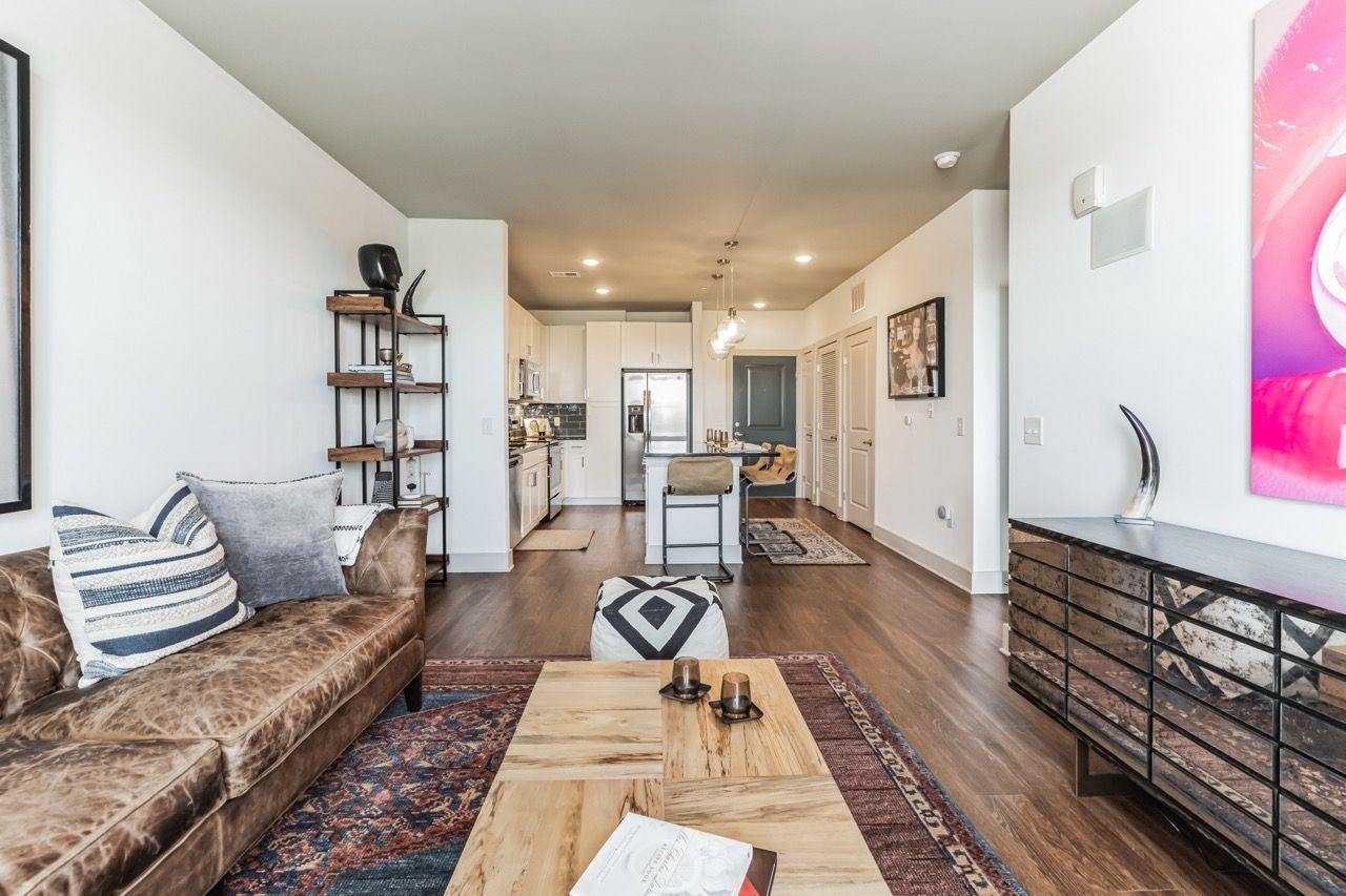 Open-concept living room with a brown leather sofa and kitchen visible in the background.