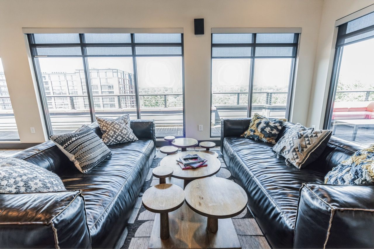 Bright living room with two black leather sofas, round coffee tables, and large windows opening to a balcony.