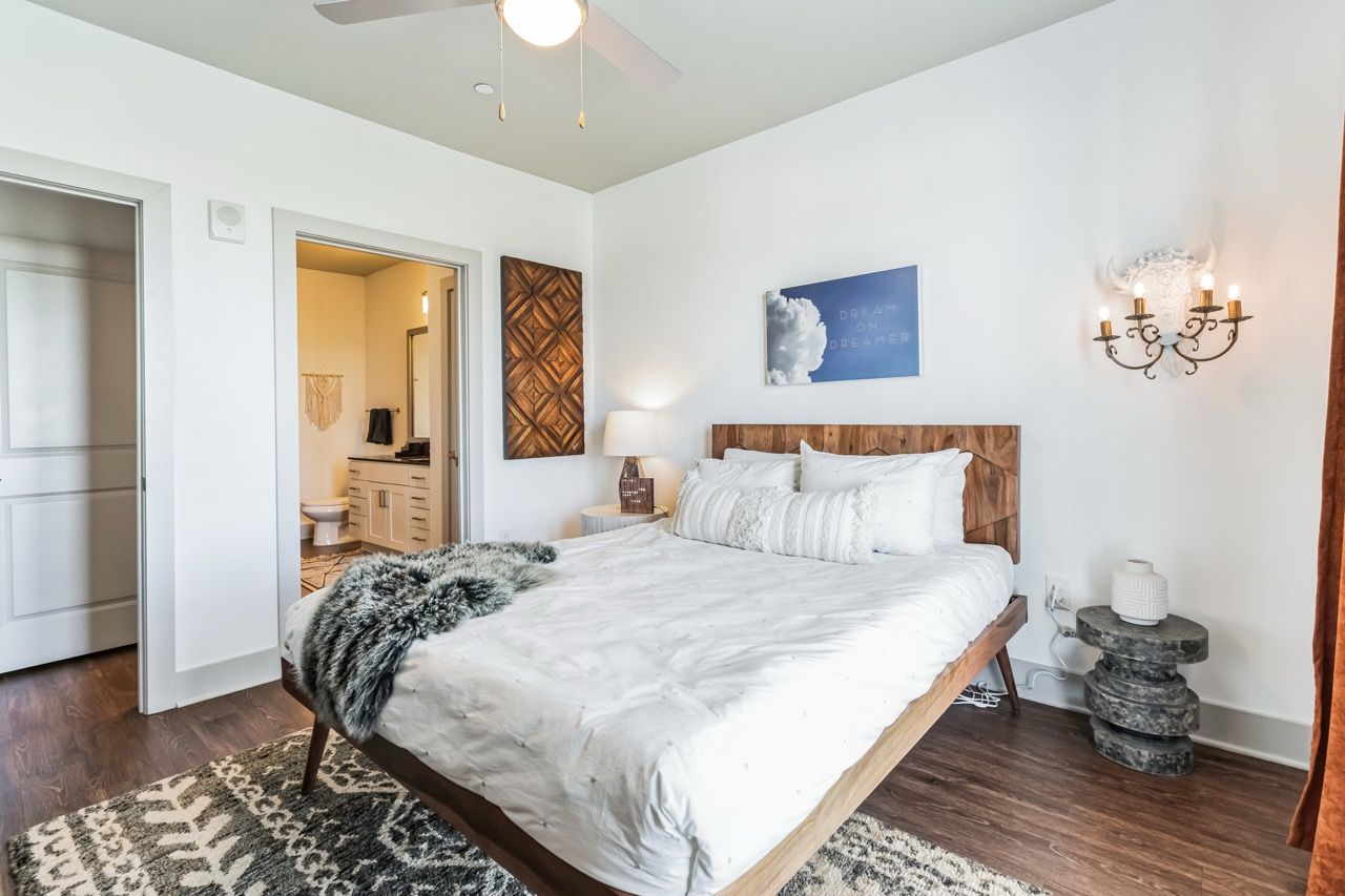 Bedroom in an apartment with a wooden headboard bed, white bedding, and an open doorway to the bathroom.