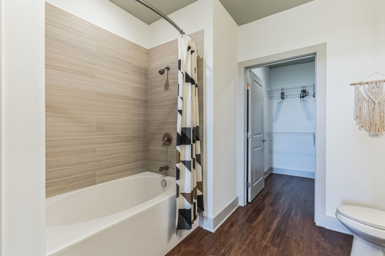 Apartment bathroom with tub/shower, beige tile surround, shower curtain, and adjacent walk-in closet.