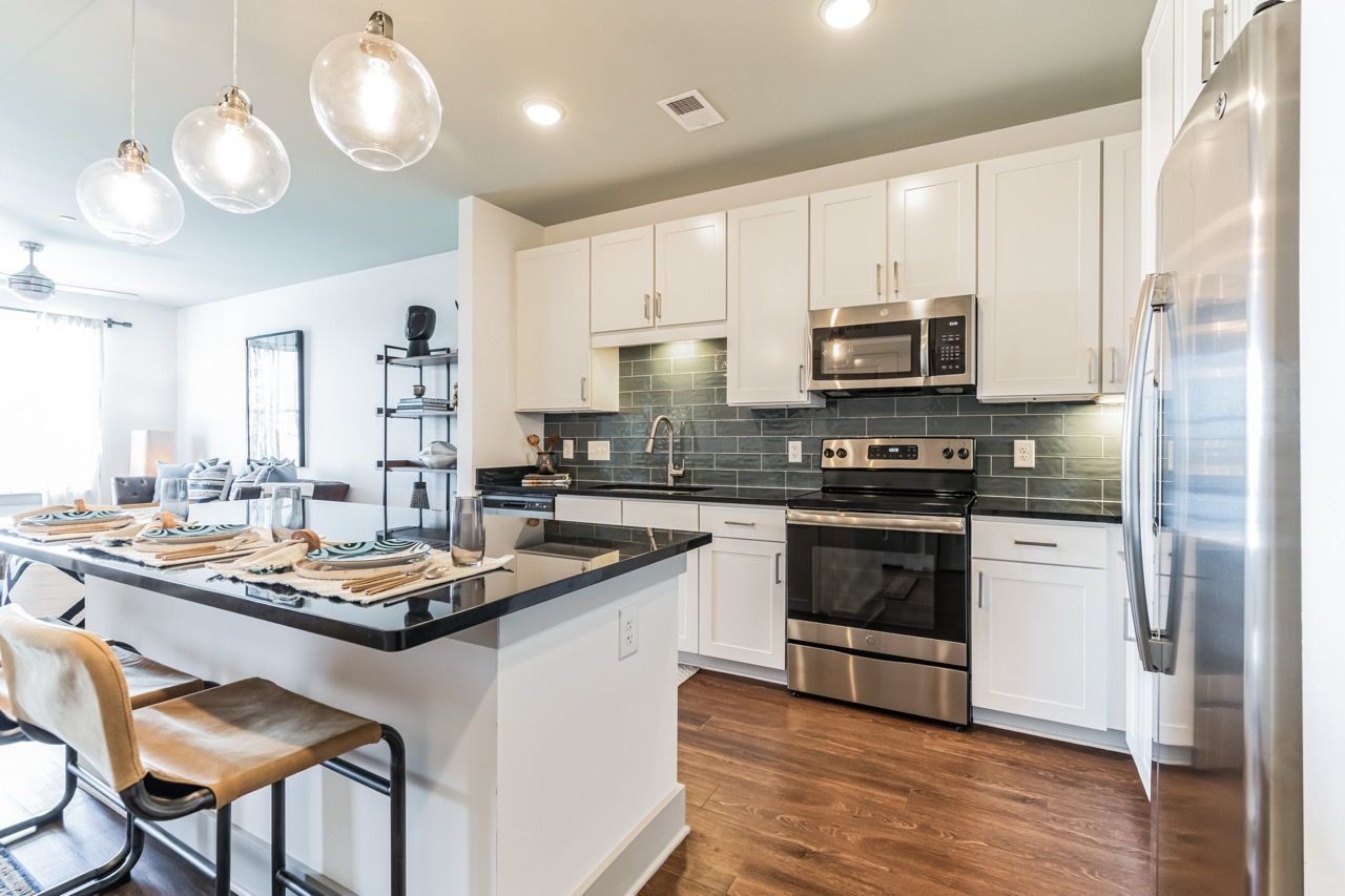 Modern apartment kitchen with white cabinets, stainless steel appliances, and a dark countertop island.
