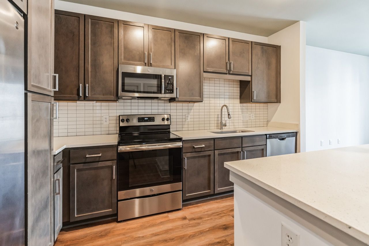 Modern kitchen with dark wood cabinets, stainless steel appliances, white countertop, and tiled backsplash.