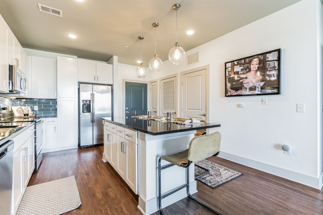Modern kitchen with island, pendant lights, stainless appliances, and hardwood floors.