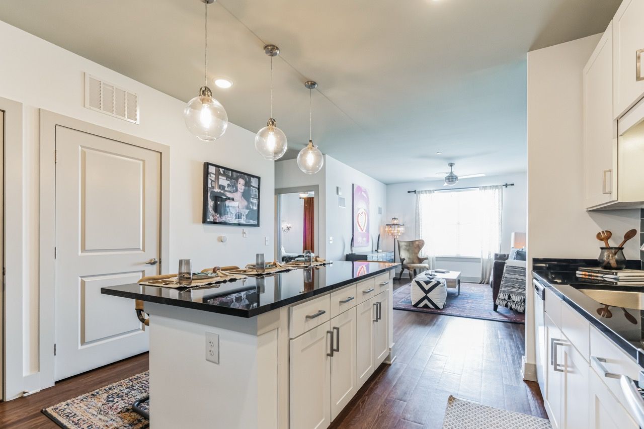 Open-concept kitchen with an island, pendant lights, and a living area in a modern apartment.