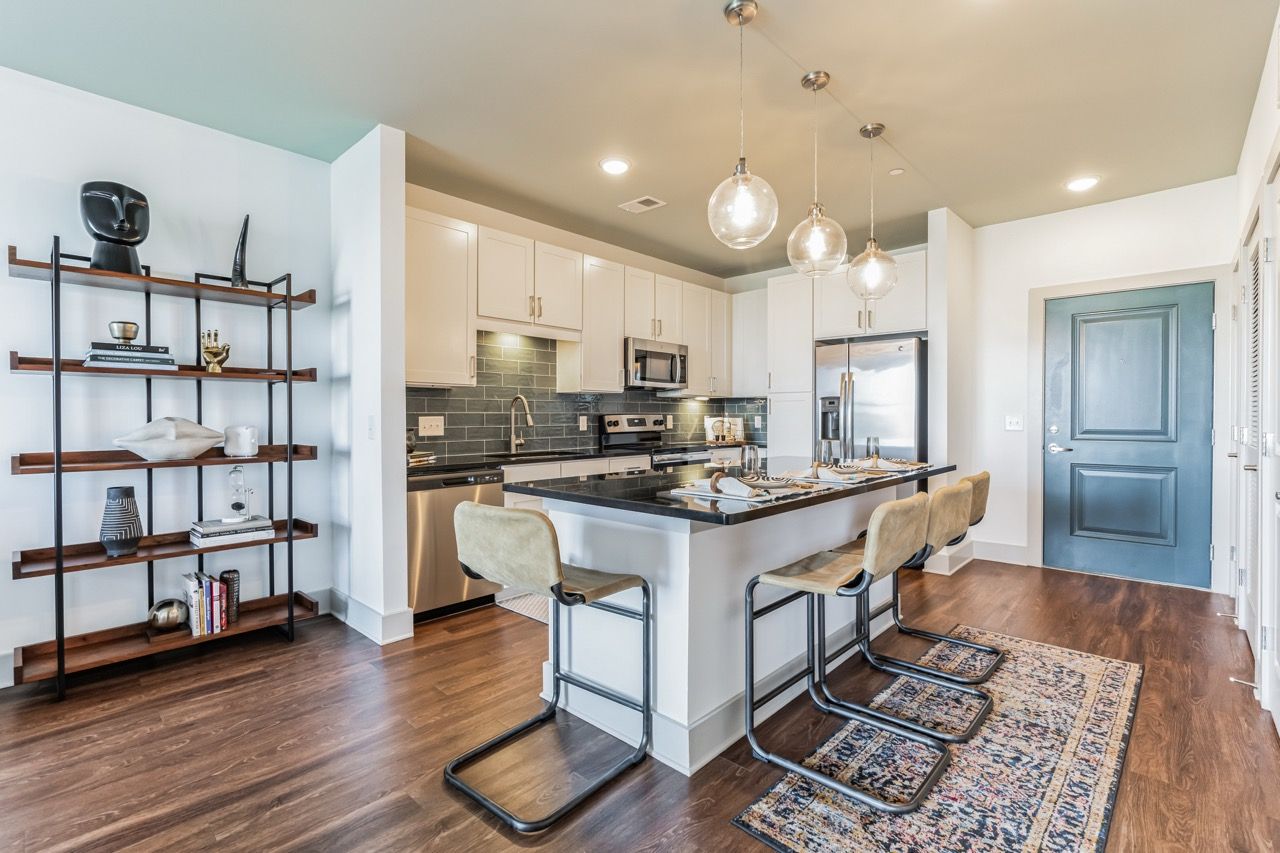 Open-concept kitchen with white cabinets, island, pendant lights, and stainless steel appliances.