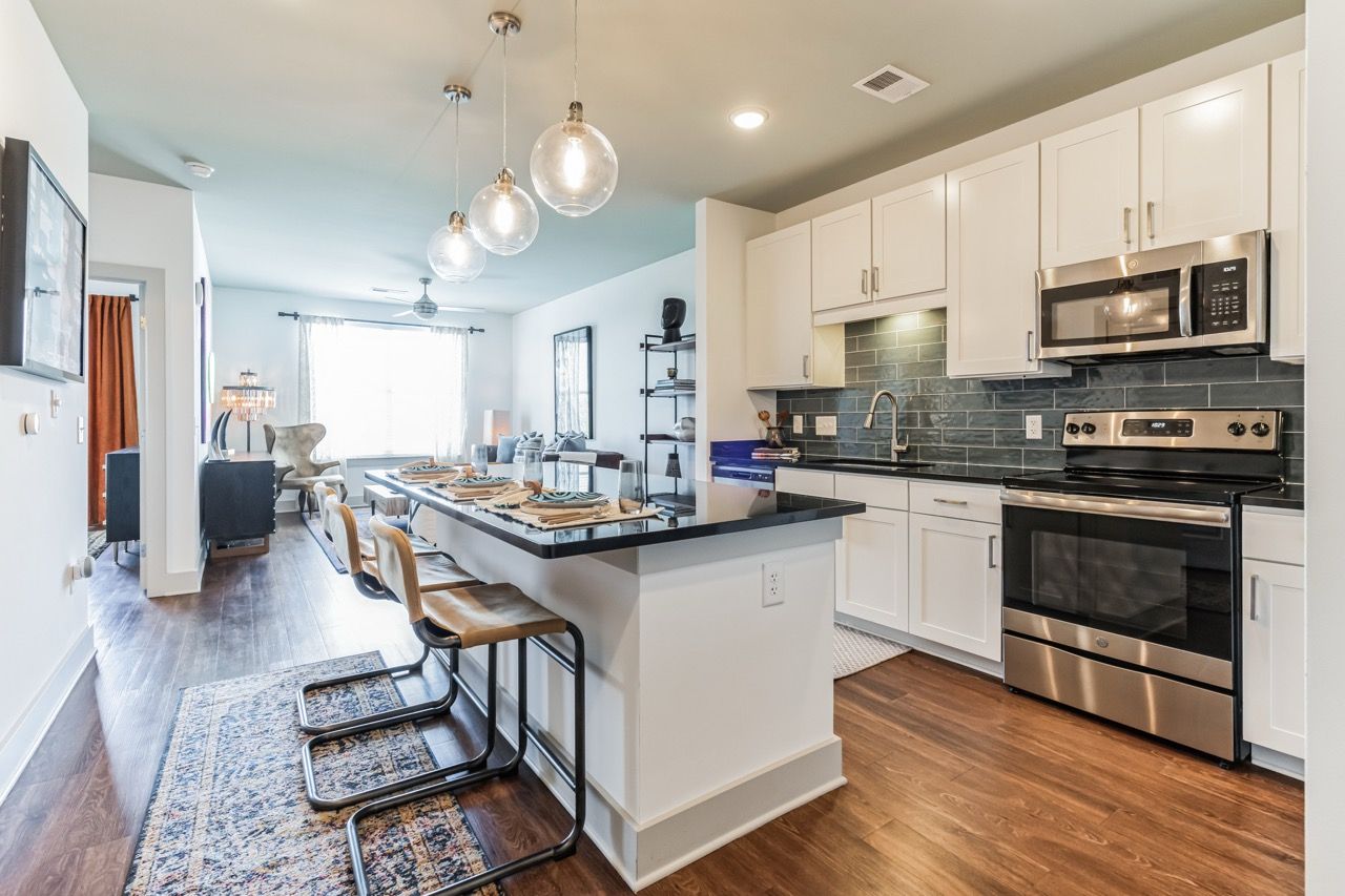 Open-plan kitchen with white cabinets, stainless steel appliances, an island with seating, and pendant lights.