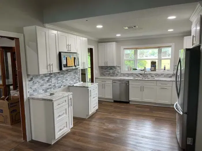 White kitchen with cabinets, appliances, and marble countertops, brown flooring.