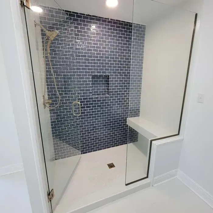 A modern bathroom shower with blue tile, glass doors, a bench, and gold fixtures.