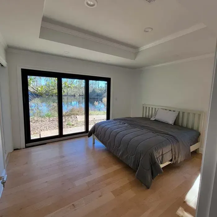 Bedroom with a white bed, gray comforter, sliding glass doors, and a view of the water.