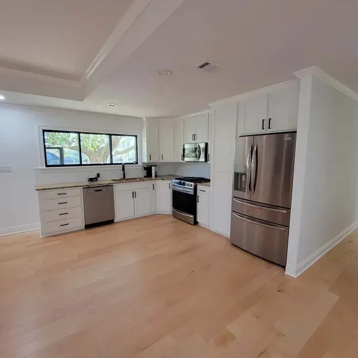 Modern kitchen with white cabinets, stainless steel appliances, and light wood floors.