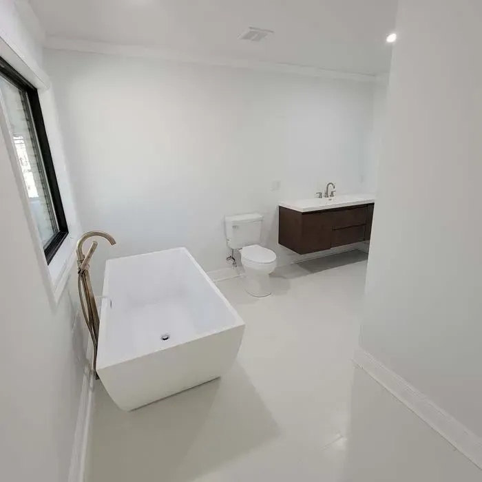 Modern white bathroom with a freestanding tub, toilet, vanity, and window.