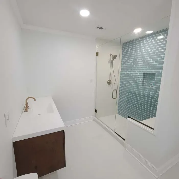 Modern bathroom: white walls, vanity with gold faucet, teal tile shower, and glass door.