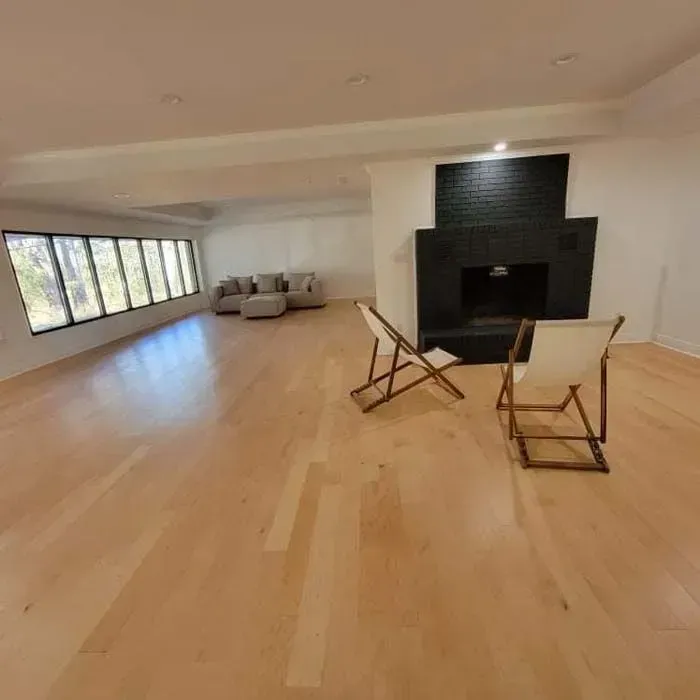 Spacious living room with hardwood floors, large windows, a black fireplace, and folding chairs.