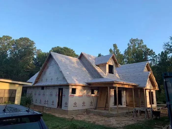 House under construction, wood frame, gray roof, brown siding, small windows, porch, clear sky.