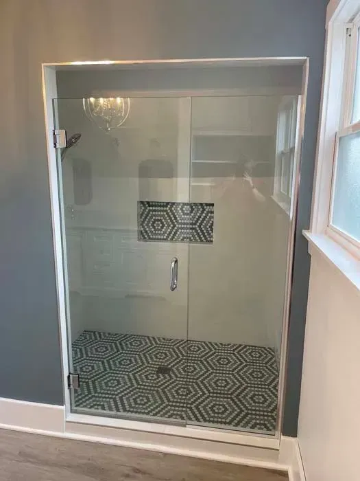 Glass shower with white frame, grey walls, and patterned floor and inset.