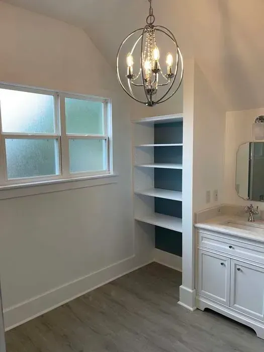 Bathroom with built-in shelves, window, vanity, and a decorative chandelier. White walls, grey floor, and blue shelf backing.