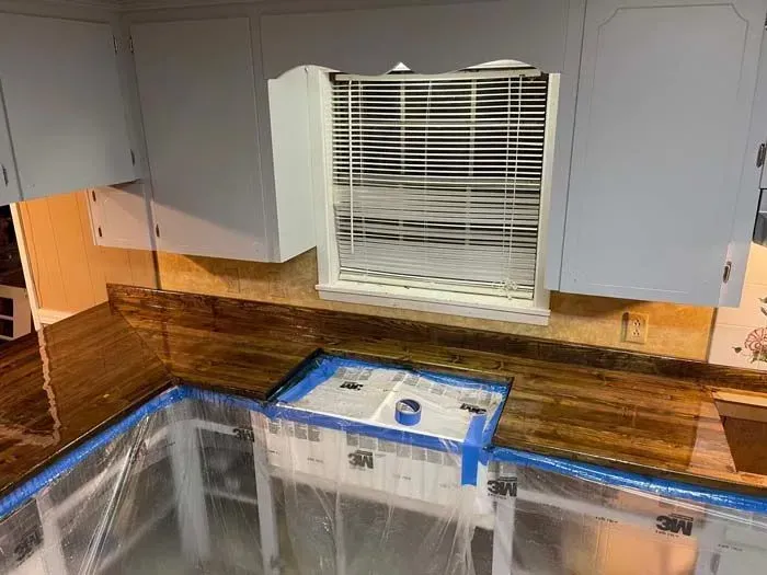Kitchen with wooden countertops, painted blue cabinets, and a fan in the window; preparing for a project.