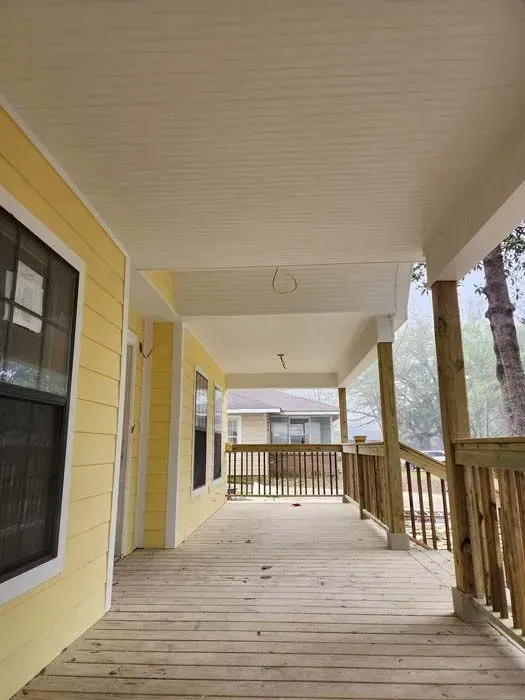 Yellow house with a covered wooden porch and railing, overlooking a yard.