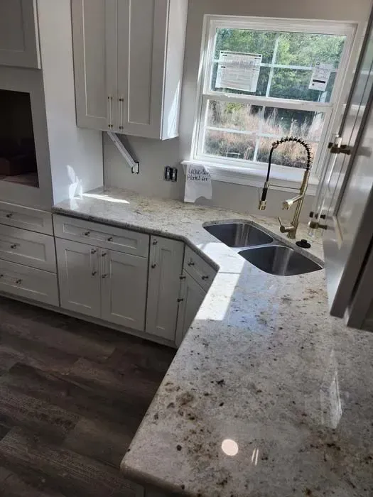 White kitchen with granite countertops, cabinets, sink, and window overlooking nature.